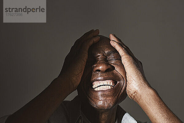 Älterer Mann lacht  während er sein Gesicht im Studio verdeckt