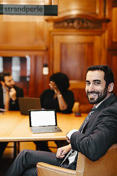 Porträt eines lächelnden  bärtigen männlichen Finanzberaters  der an einem Konferenztisch im Sitzungssaal sitzt