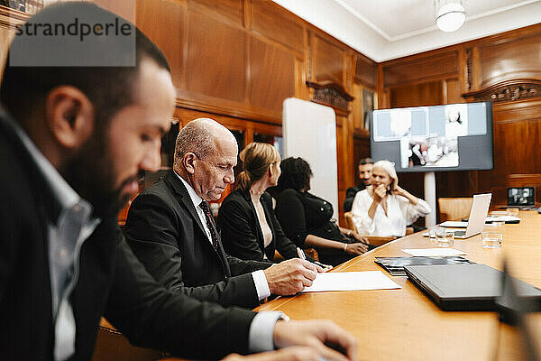 Männlicher Finanzberater bei der Unterzeichnung eines Vertrags während einer Sitzung mit Kollegen im Sitzungssaal