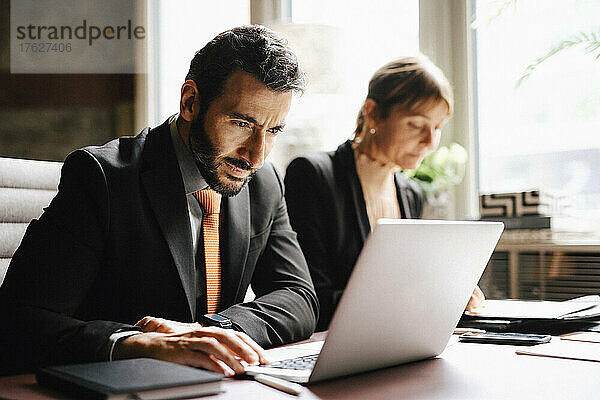 Geschäftsmann mit Laptop  der neben einer Geschäftsfrau am Schreibtisch in einer Anwaltskanzlei arbeitet