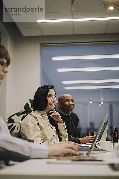 Lächelnde Geschäftsfrau mit männlichen und weiblichen Kollegen  die sich bei der Arbeit im Büro unterhalten