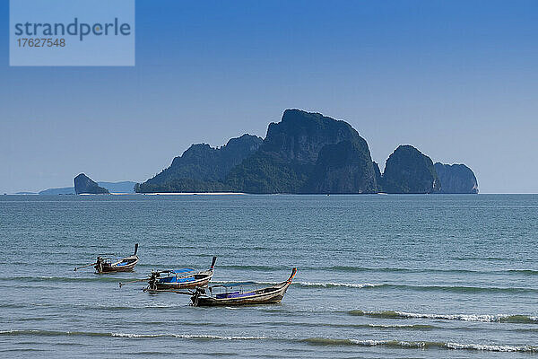 Lange Boote vertäuten am Strand von Ao Nang mit der dahinter liegenden Insel.