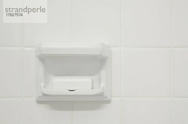 Eine weiß geflieste Wand eines Badezimmers oder Duschraums mit einer geformten Aussparung aus Porzellan. Ein Block Seife.