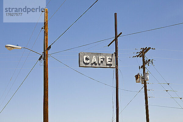 Café-Schild hoch oben an einer Stange  Strom- und Telefonleitungen an Pfosten.