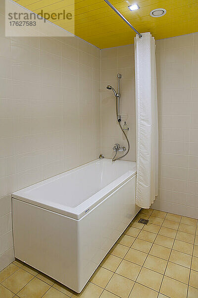 Ein Badezimmer  Badewanne und an der Wand montierte Dusche und Duschvorhang  Fliesenboden und gelbe Decke.