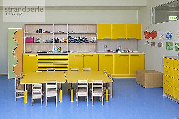 Klassenzimmer in einem Kindergarten  gelbe Möbel und Tische und blauer Boden.