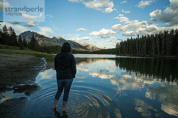 Frau steht im seichten Wasser des Johnson Lake im Banff-Nationalpark und blickt auf Berge und ländliche Szenerie.