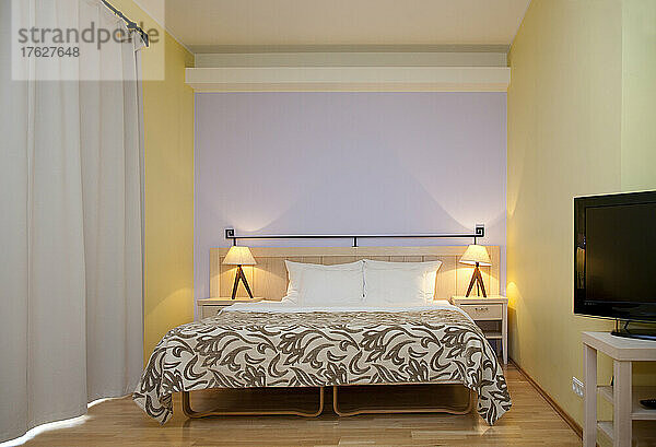 Ein Hotelzimmer  moderne Möbel und Einrichtung  Doppelbett und Nachttischlampen  Fernseher und lange weiße Vorhänge.
