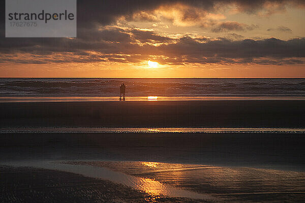 Paar umarmt sich am Cannon Beach mit dramatisch bewölktem Himmel bei Sonnenuntergang.