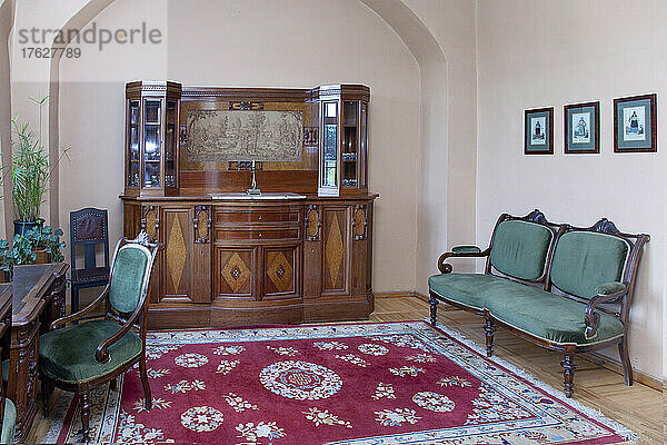 Eine große antike Vitrine  Stauraum  ein Teppich sowie Stühle und Schreibtisch im antiken Stil in einem Raum