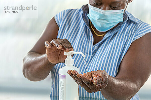 Coronavirus. Geschäftsfrau  die von zu Hause aus arbeitet und eine Schutzmaske trägt  weil sie eine Schutzmaske trägt. Reinigt ihre Hände mit Desinfektionsgel.