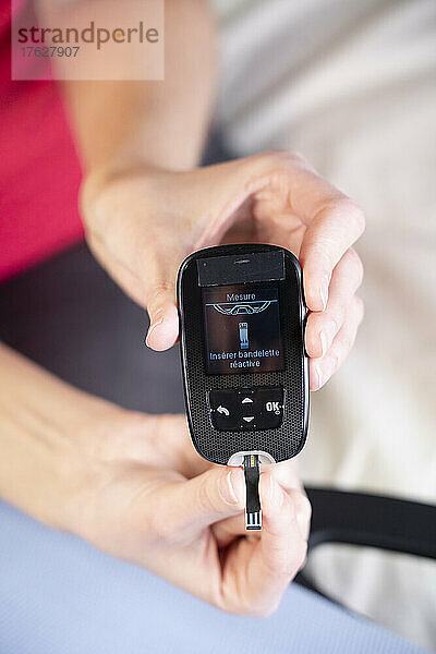 Nahaufnahme der Hände einer Diabetikerin  die einen Tab in ein Gerät einführt  um ihren Blutzuckerspiegel zu messen.