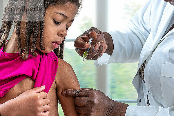 Kleines Mädchen schaut auf seinen Arm  während es geimpft wird