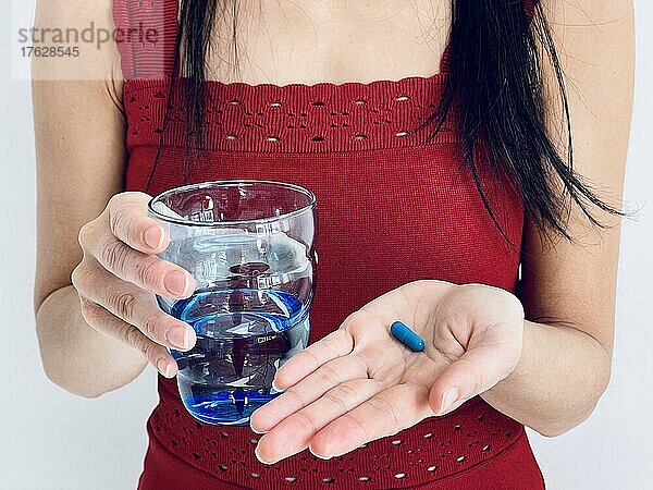 Hände halten ein Glas Wasser und eine Pille.