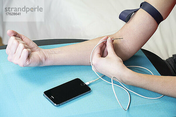 Nahaufnahme des Arms einer Frau  die sich über ein Smartphone eine Injektion verabreicht.