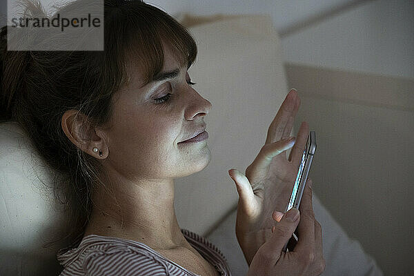 Frau bewundert nachts ihr beleuchtetes Smartphone. Suchtverhalten.