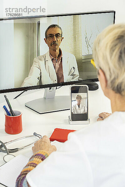 Nahaufnahme einer Telekonsultation zwischen zwei Ärzten  von denen einer mit seinem Telefon gefilmt wird.
