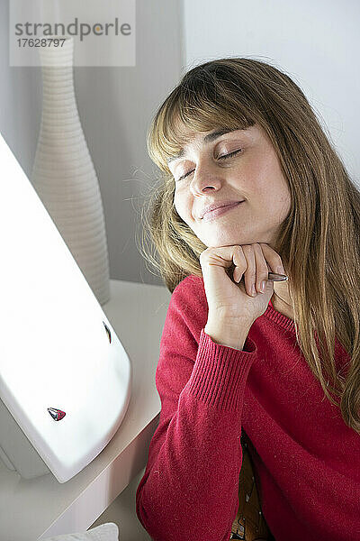 Frau sitzt mit ihrem Tagebuch neben einer Lichttherapielampe.