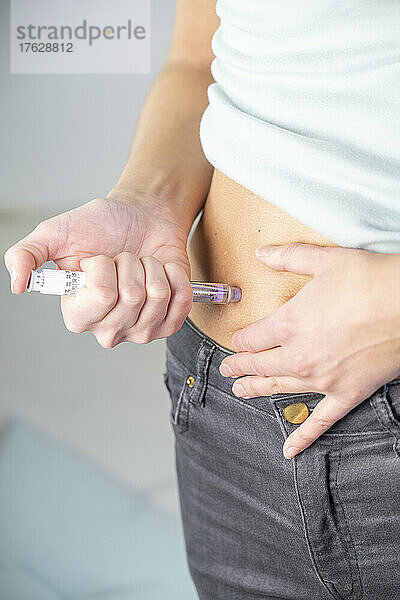 Nahaufnahme der Hände und des Bauches einer Frau  die sich selbst eine Insulinspritze gibt.