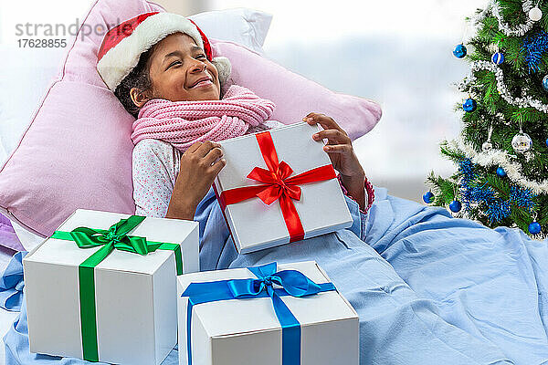 Kleines Mädchen mit Weihnachtsmütze erhält ihr Geschenk  während sie im Krankenhaus ist