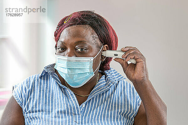 Fieber- und Coronavirus-Symptome  Frau in medizinischer Maske misst Körpertemperatur.