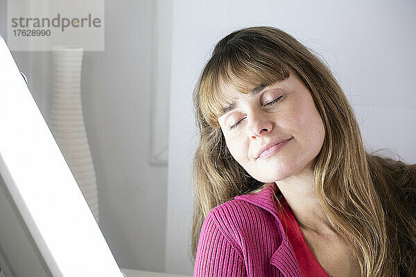Woman sitting near a white light lamp for light therapy.