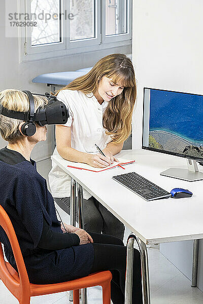 Ältere Frau während einer Therapiesitzung mit einem Virtual-Reality-Headset unter Aufsicht eines Therapeuten.
