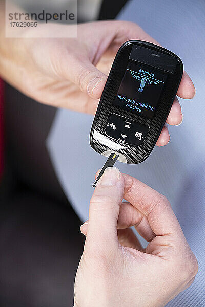 Nahaufnahme der Hände einer Diabetikerin  die einen Tab in ein Gerät einführt  um ihren Blutzuckerspiegel zu messen.