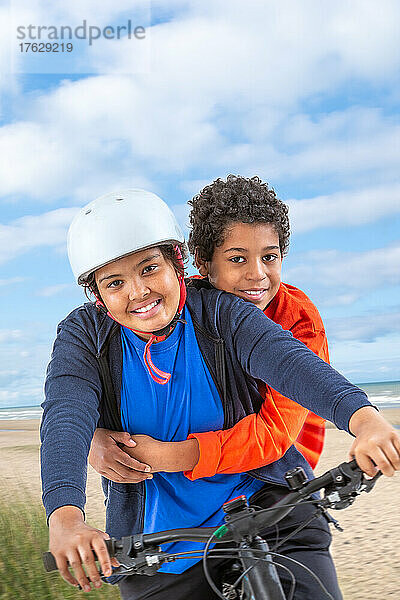 Zwei Teenager-Jungen und -Mädchen fahren Fahrrad am Strand
