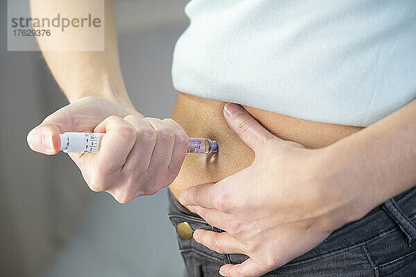 Nahaufnahme der Hände und des Bauches einer Diabetikerin  die sich selbst eine Insulinspritze gibt.