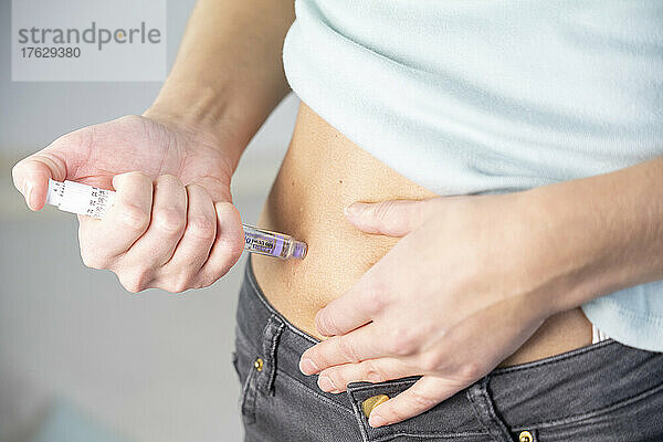 Nahaufnahme der Hände und des Bauches einer Diabetikerin  die sich selbst eine Insulinspritze gibt.