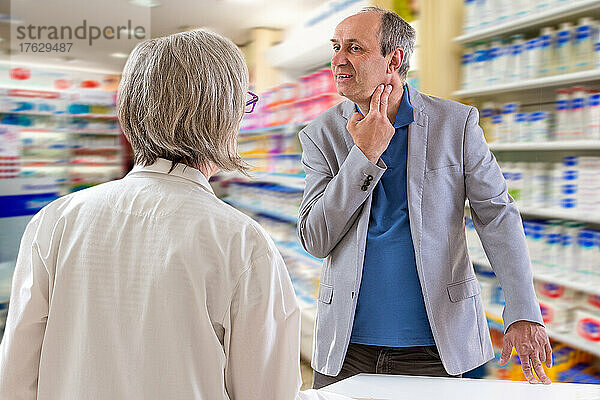 Apotheker spricht mit einem Mann  der Halsschmerzen hat.