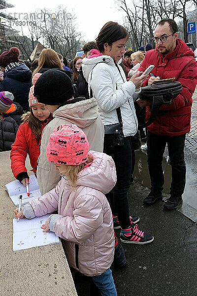 Ukrainische Flüchtlinge vor der Botschaft der Ukraine – Bukarest – Rumänien  um einen biometrischen Reisepass zu erhalten. Kinder zeichnen Kriegsszenen in ihre Notizbücher  während sie mit ihren Eltern darauf warten  in der Botschaft empfangen zu werden.