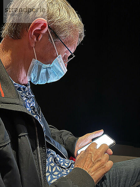 Mann mit Maske und Brille im Profil blickt auf sein Smartphone. Paris  Ile-de-France  Frankreich.