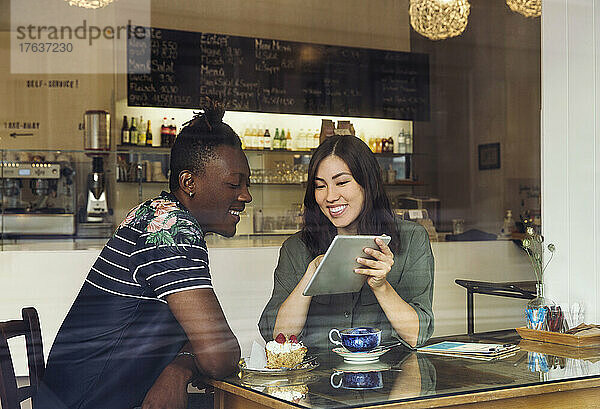 Lächelndes Paar schaut im Café auf ein digitales Tablet