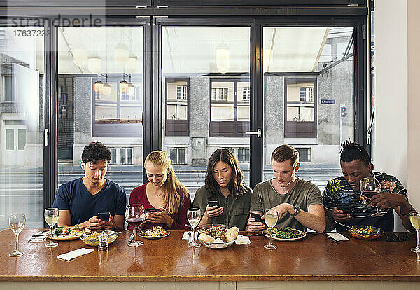 Freunde essen im Restaurant und schauen auf Smartphones