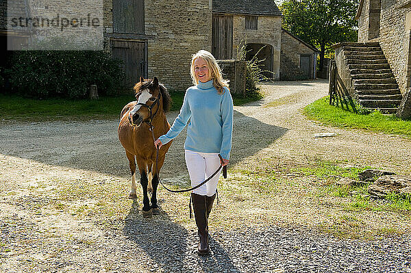Lächelnde Frau geht mit Pony auf dem Bauernhof spazieren