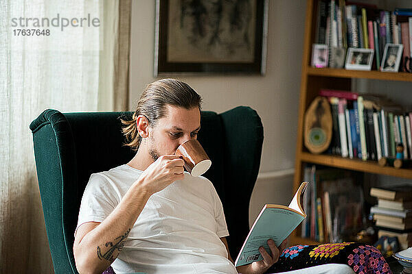 Mann trinkt Kaffee und liest ein Buch im Sessel