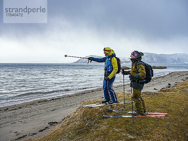Bergführer deutet seinem Gast das nächste Ziel  Skitour endet am Strand  Senja  Troms  Norwegen  Europa