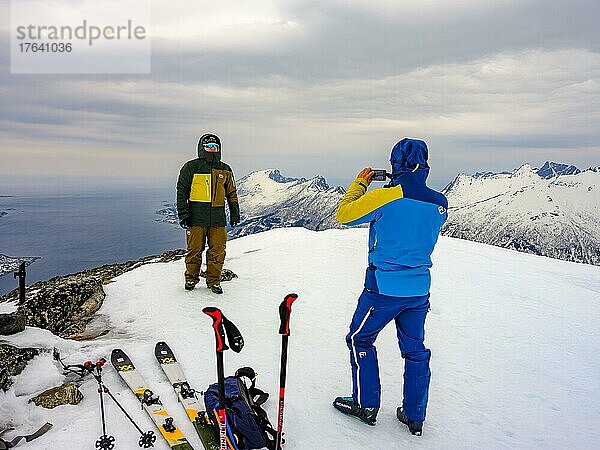 Skibergsteiger mit Handi macht ein Gipfelfoto auf dem Flobjörn mit Blick auf das Meer  Insel Senja  Troms  Norwegen  Europa