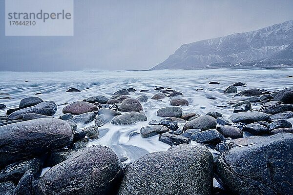 Waves of Norwegian sea surging on stone rocks at Unstad beach  Lofoten islands  Norway in winter storm. Long exposure