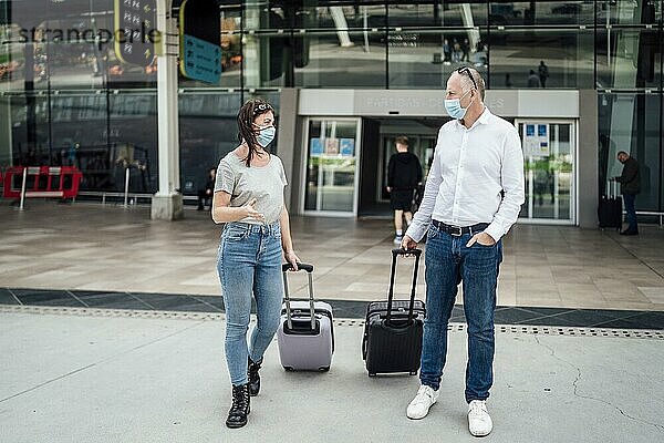 Ein paar Freunde mit Schutzmasken unterhalten sich beim Verlassen des Flughafens mit ihrem Gepäck
