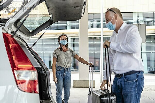 Ein Taxi- oder Uber-Fahrer hilft einem Fahrgast mit Schutzmaske am Flughafen mit seinem Gepäck