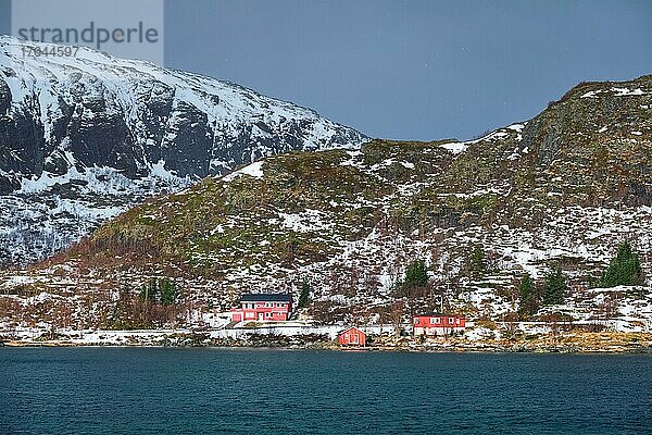 Traditional red rorbu houses on fjord shore in snow in winter. Lofoten islands  Norway