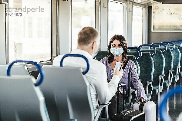 A couple of friends wearing mask and nicely talking while traveling by train