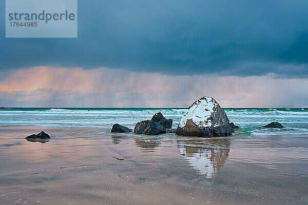 Rocks covered with snow on Norwegian sea beach in fjord in stormy weather with clouds. Skagsanden beach  Flakstad  Lofoten islands  Norway. Long exposure motion blur