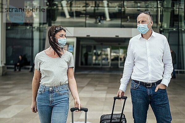 Ein paar Freunde mit Schutzmasken unterhalten sich beim Verlassen des Flughafens mit ihrem Gepäck