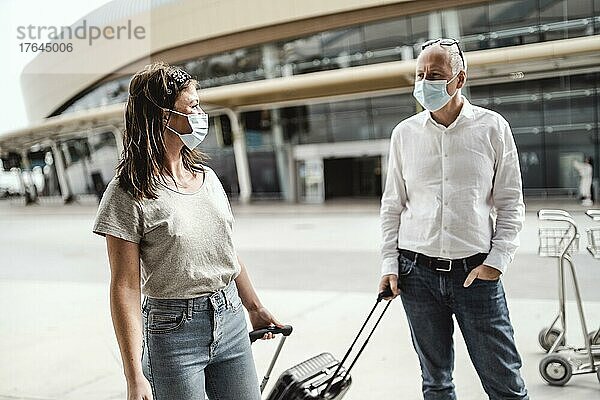 Ein paar Freunde mit Schutzmasken unterhalten sich beim Verlassen des Flughafens mit ihrem Gepäck