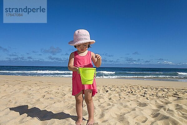 Toddler girl holding a green bucket at the beach  Kauai island  Hawaii