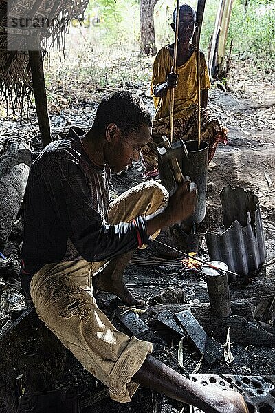 Archaische Schmiede  Handwerker schmiedet unter einem Dach Eisennägel über offenem Feuer  das mit Blasebalg angefacht wird  Unguja  Sansibar  Tansania  Afrika